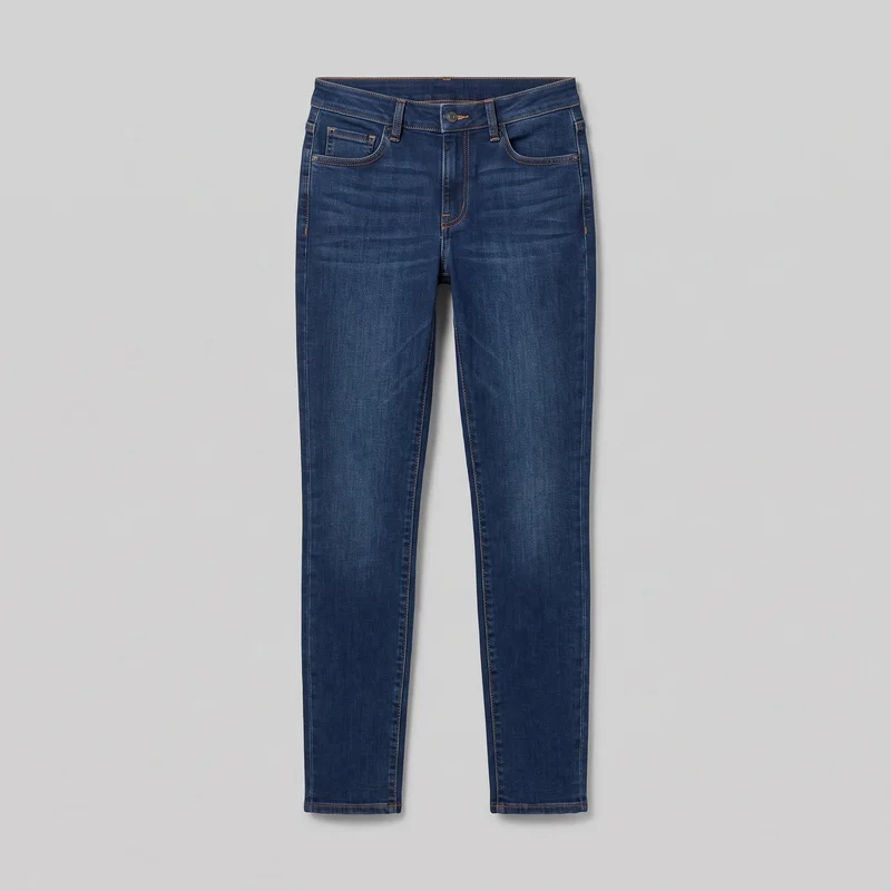 Women's indigo slim-fit jeans shown as a complete front flat view, including the structured waistband with belt loops, central button, fly placket, curved front pockets, coin pocket, pocket-corner rivets, and visible side seams. The full-length legs have narrow tapered cuts, straight hems, contrast topstitching, and lightly varied wash and fading across the thighs and legs.