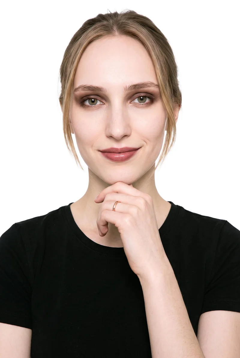 An 18-year-old Slavic woman is shown in a front-facing bust crop with her wrist raised beside her jaw, presenting a women's rose gold band. She is smiling against a pure white backdrop.