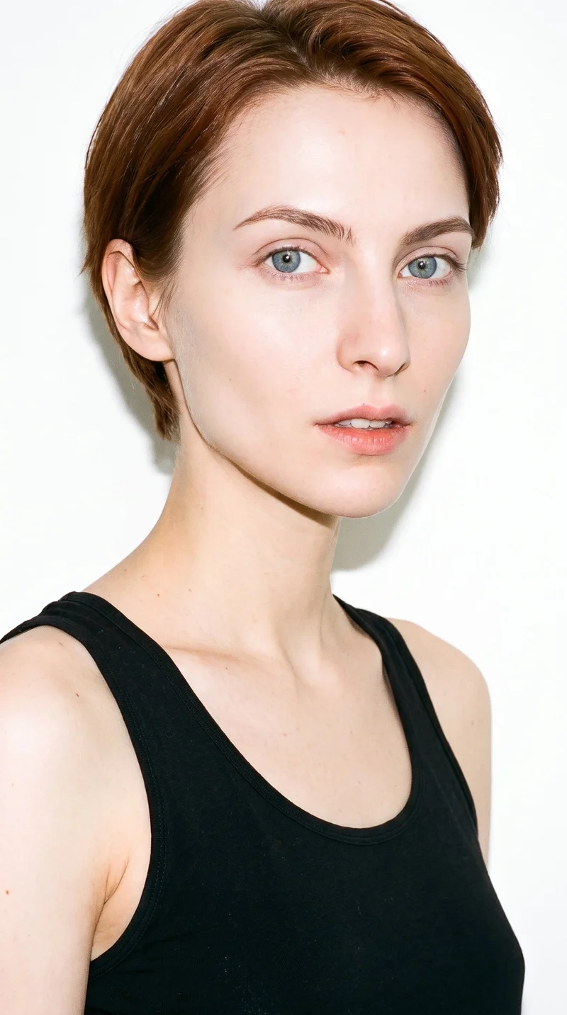 This 24-year-old Slavic woman has porcelain skin with a cool undertone and a doll-like face formed by large, even features and soft, rounded proportions. Her eyebrows are medium in thickness, and her eyes are blue with a cool undertone. She has medium-sized lips and short, even reddish-brown hair with a warm tone. No facial hair is recorded.