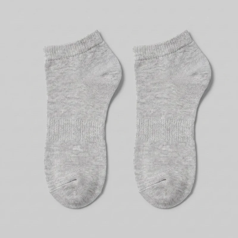 A complete pair of grey low-cut cotton ankle socks is shown flat side by side. The socks have slim foot-hugging silhouettes, rounded closed toes with visible seam arcs, shaped heel pockets, short ribbed cuffs, and low openings that sit below the ankle. Fine knit texture and denser rib-knit zones are visible through the cuffs and parts of the foot, with no visible logos, prints, patches, embroidery, or embellishments.