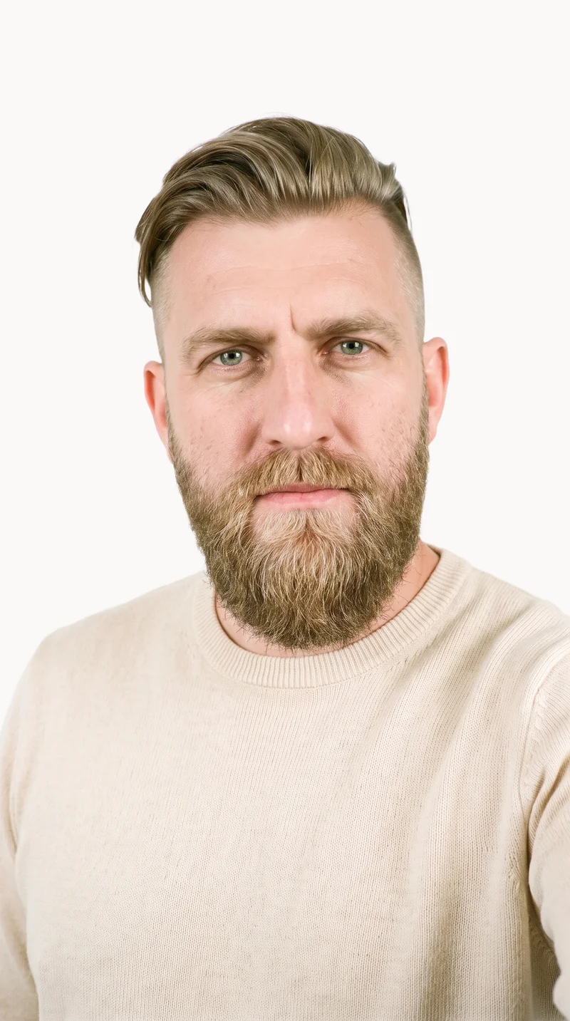 A 43-year-old Slavic man wears a cream cashmere knit in a front-view selfie, with his chin lowered and a soft expression. A Chantilly Lace flat-color backdrop fills the background.