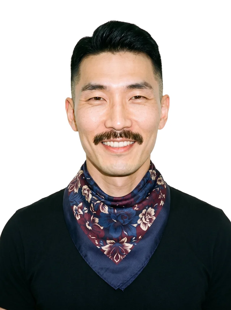 A 46-year-old Korean man models a men's floral print silk scarf in a front-facing bust composition with his head level and a natural expression. The scarf is shown against a pure white backdrop.