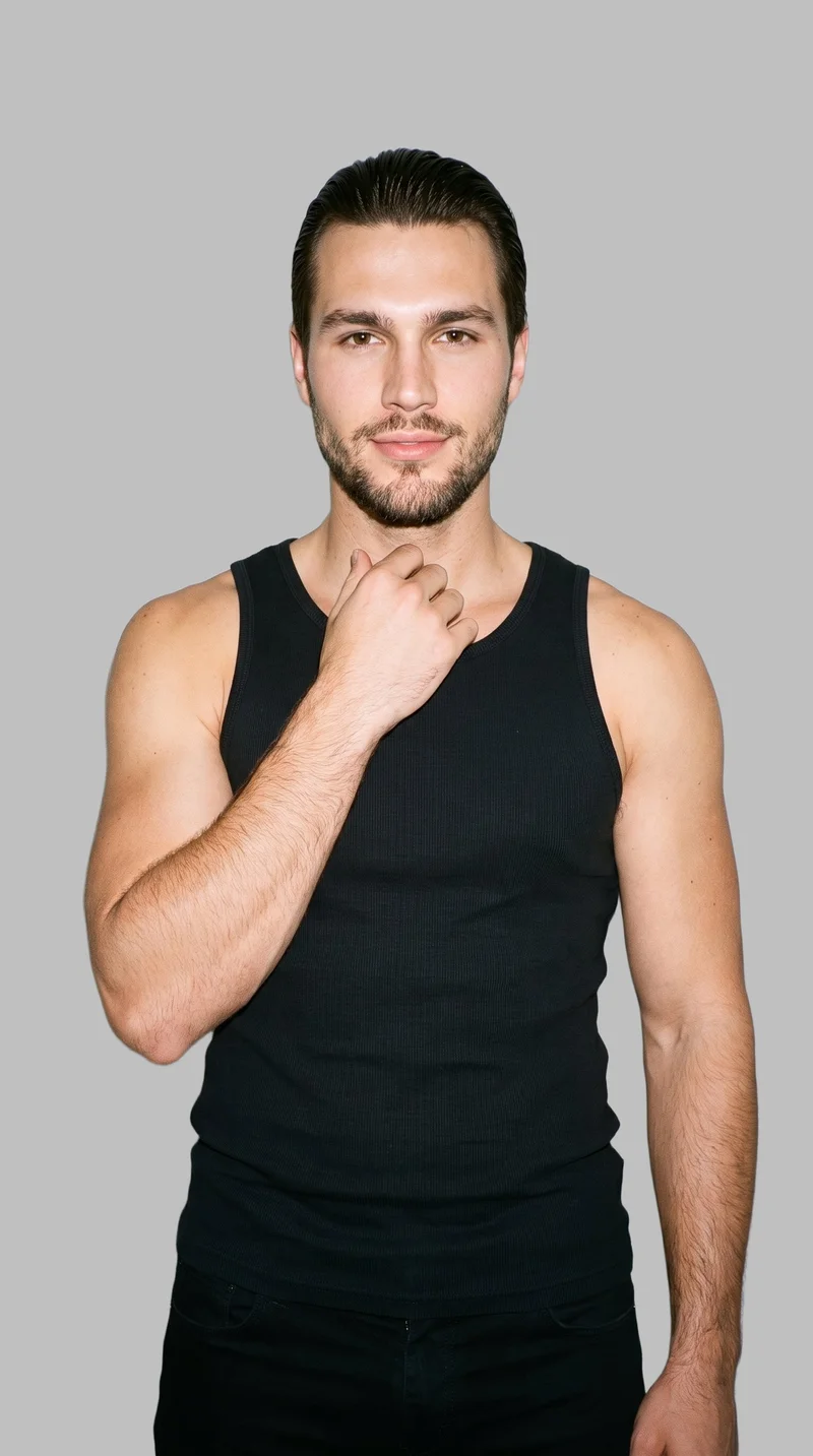A 26-year-old Caucasian male model wears a black ribbed tank top in an upper-body, front-view composition, with one hand at his collarbone and a natural expression. A flat Silver Mist backdrop surrounds the studio-cutout presentation.