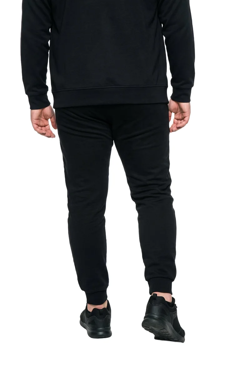 The lower body of a male model wearing a men's black tracksuit is shown from the rear, with one heel lifted. The figure is isolated against a pure white backdrop.