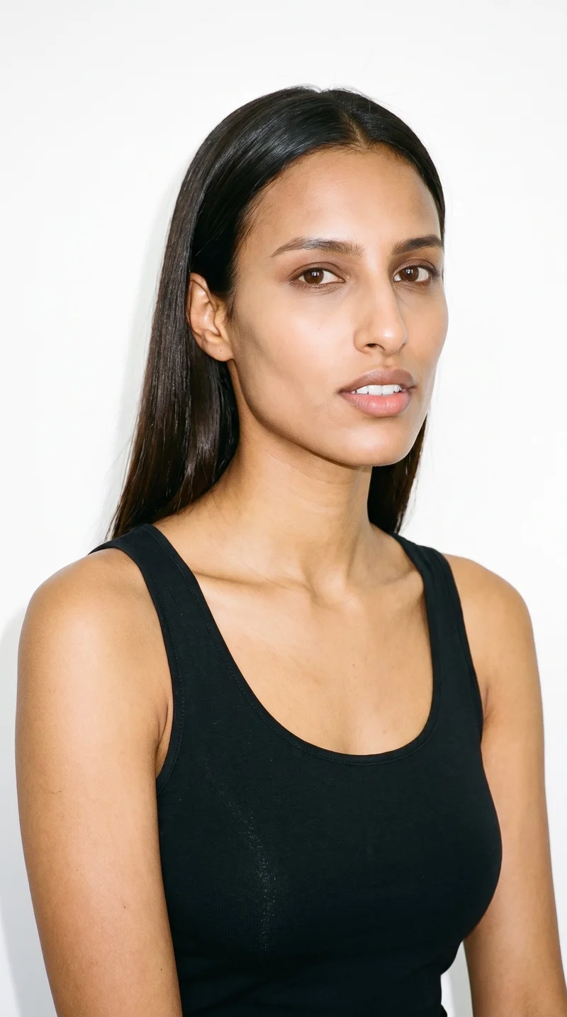 This 24-year-old Arab woman has warm honey-toned skin with an olive-green undertone. Her square face has a broad forehead and a strong, defined jaw, giving it an angular, structured appearance. She has medium-thickness eyebrows, brown eyes, and full lips. Her dark-brown hair is straight, smooth, and divided evenly at the centre.