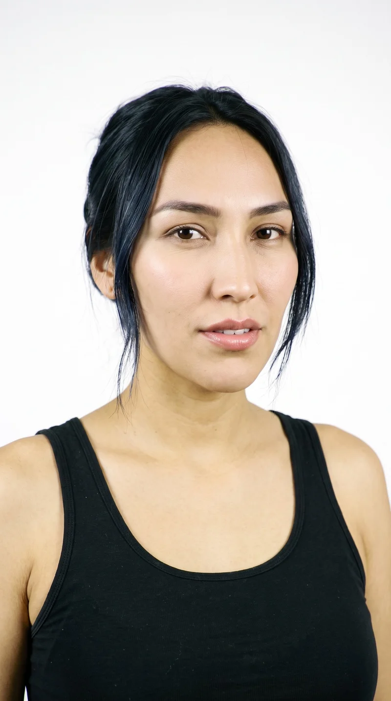 A 25-year-old woman with an Indigenous American appearance and medium olive skin with a warm, greenish-golden undertone. Her face is long, with more length than width, a tall forehead, and elongated cheeks. She has thick eyebrows, very dark near-black eyes, and medium lips. Her deep black hair is twisted up and secured with a claw clip, with relaxed ends.