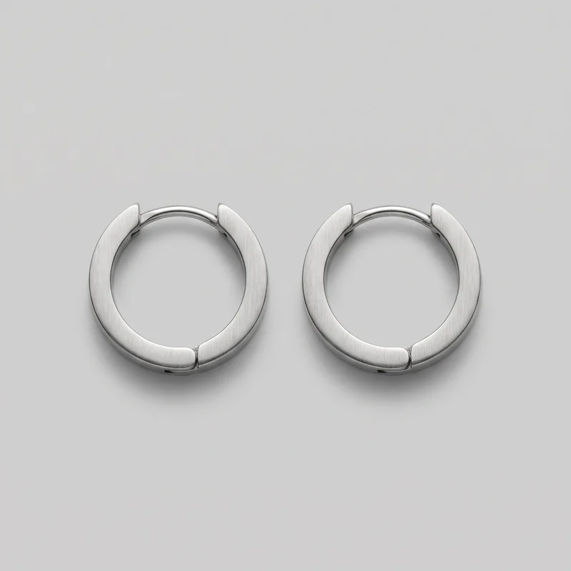 A matched pair of circular hinged hoop earrings is shown as a standalone product. The full ring shapes, flattened outer faces with fine vertical brushing, lower-front pivot seams, and top fastening posts are visible.