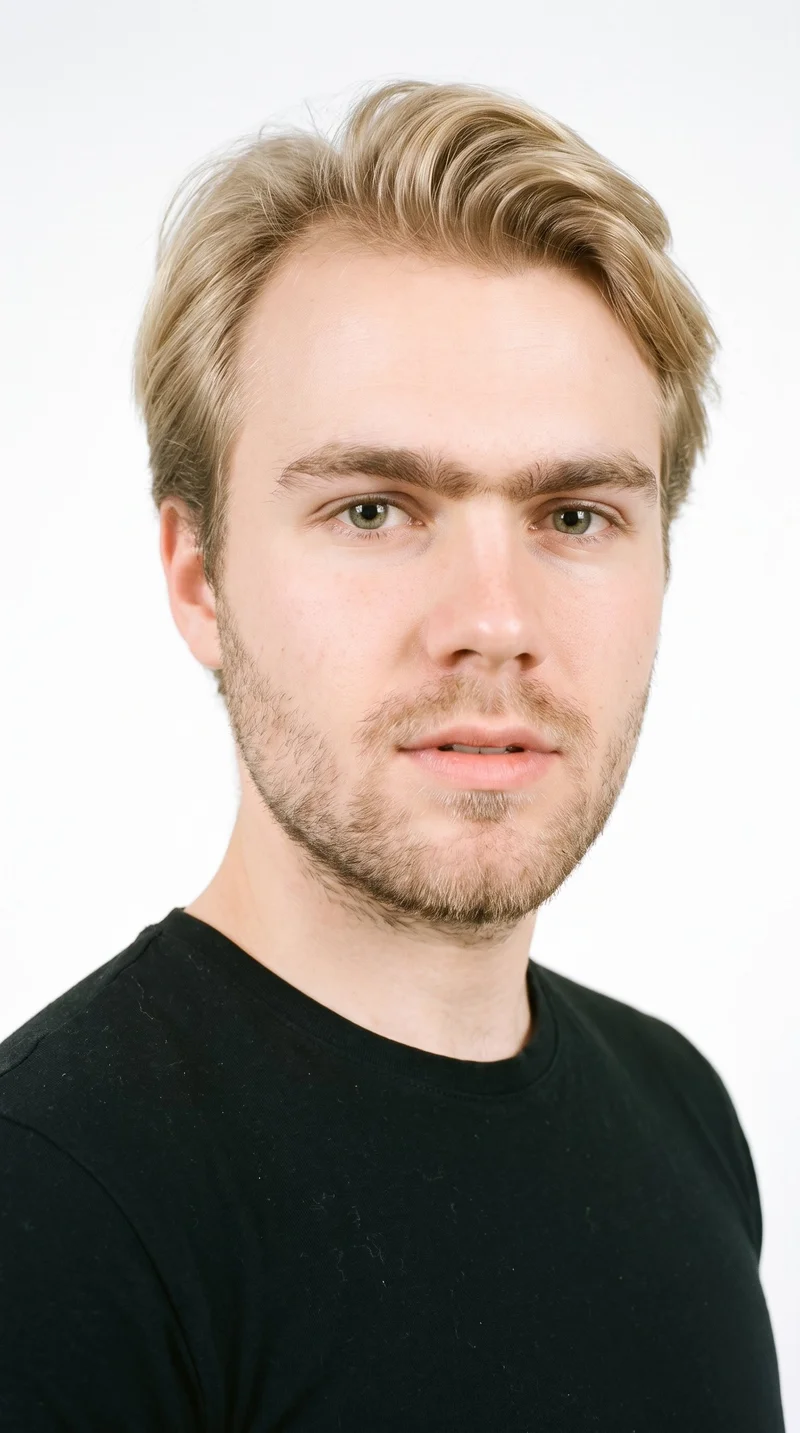 A 21-year-old Caucasian man with fair skin and a neutral undertone has a round face with soft, full contours and few angles. His thick eyebrows frame hazel eyes with green-gold flecks, and his lips are thin. He has mid-tone blonde hair styled with longer hair on top and markedly shorter sides and back, creating a strong contrast. Dense heavy stubble forms a dark, defined layer across the beard area.