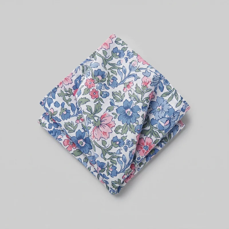 A folded square pocket square is shown as a standalone accessory. It has multiple visible layers, crisp squared edges, a narrow stitched border, and an all-over botanical print of outlined flowers, leaves, and curling stems.
