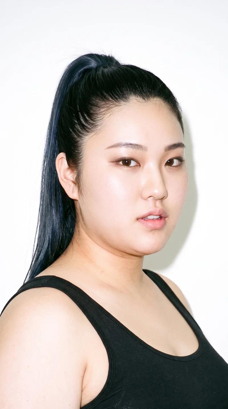 This 20-year-old Japanese woman has fair skin with a cool undertone and East Asian facial features. Her heart-shaped face has a wider forehead that narrows to a more pointed chin. She has medium-thickness eyebrows, brown eyes, and thin lips. Her black hair is pulled into a ponytail high on the crown.