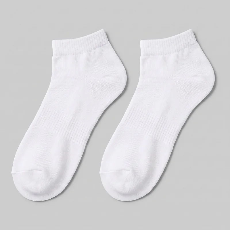 A pair of white low-cut ankle socks is shown as a standalone product. Both socks have rounded toes, defined heel pockets, short close-fitting cuffs, fine vertical ribbing through the foot and cuff, denser elastic at the openings, and shaped seam construction at the toes and heels. No logos, prints, patches, embroidery, or embellishments are visible.