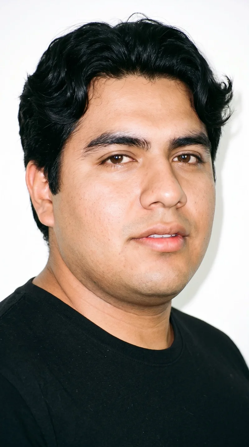 A 31-year-old Hispanic man with medium-brown skin and a warm golden undertone. His face has balanced oval proportions with a softly rounded jaw, thick eyebrows, brown eyes, and medium-sized lips. He has wavy, deep black hair and is clean-shaven, with smooth skin across his face.