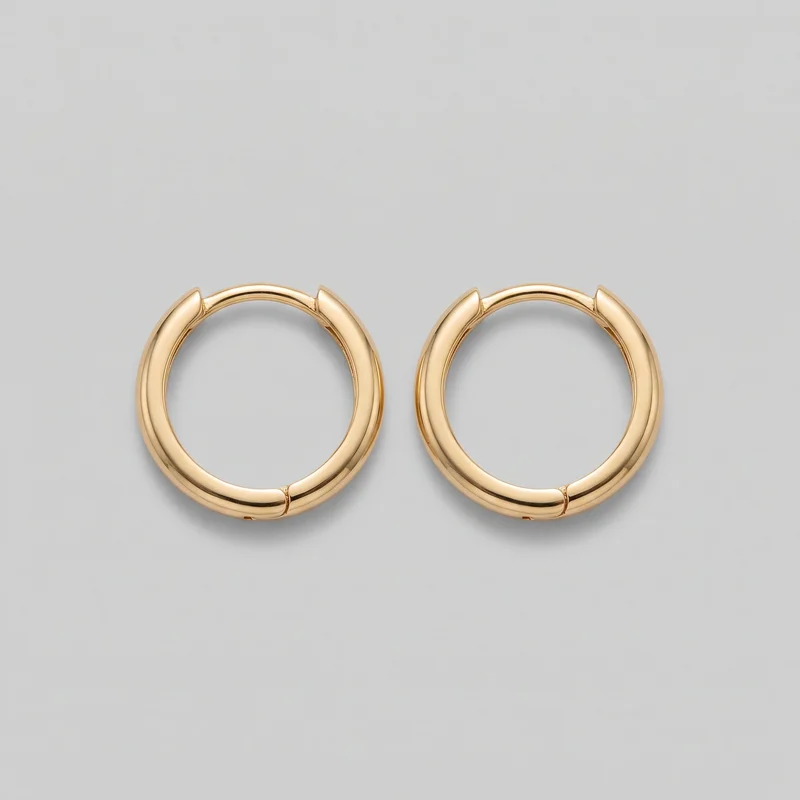 A matching pair of women's huggie hoop earrings is shown as a standalone product in a straight-on view. Each earring has an open circular silhouette with a smooth, rounded tubular profile, a visible hinge seam at the lower front, and pointed clasp ends at the top latch area. The polished surfaces are plain, with no visible logos, stones, engraving, or other embellishments.