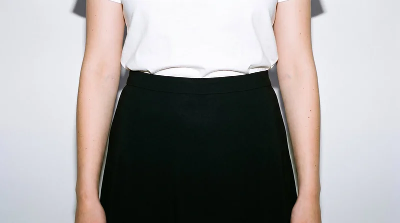 The black maxi skirt is shown from the front on a female model, framed from the hips with her hips level. A porcelain studio wall forms the backdrop.