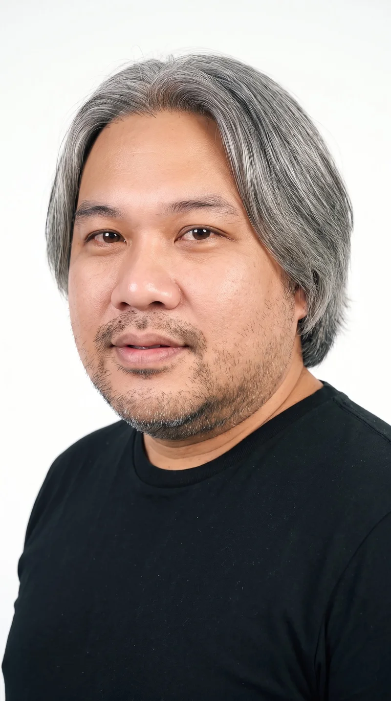 This 45-year-old Southeast Asian man has a medium skin tone with a neutral undertone and an oval face with balanced proportions and a softly rounded jaw. His eyebrows are thin, and his eyes are brown. He has medium lips, gray hair divided at the centre and falling evenly to both sides, and a short, structured boxed beard with defined edges along the cheeks and jaw.