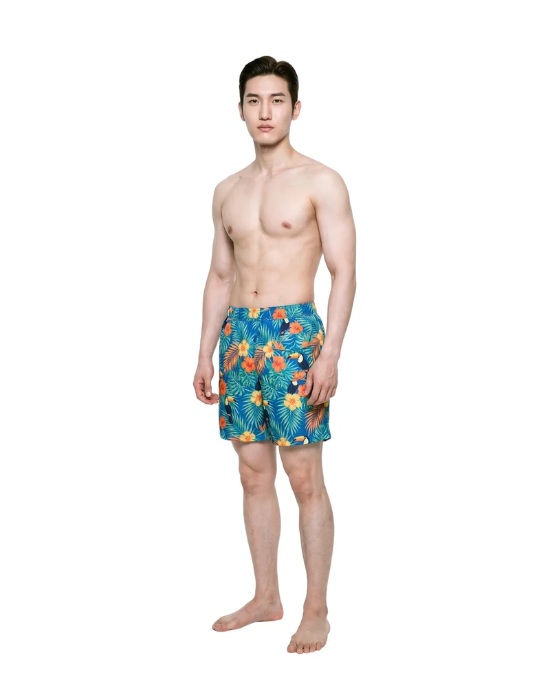 A 21-year-old Korean male model stands straight in an angled front view wearing tropical print board shorts. His neutral expression and full-body pose are shown against a pure white backdrop.