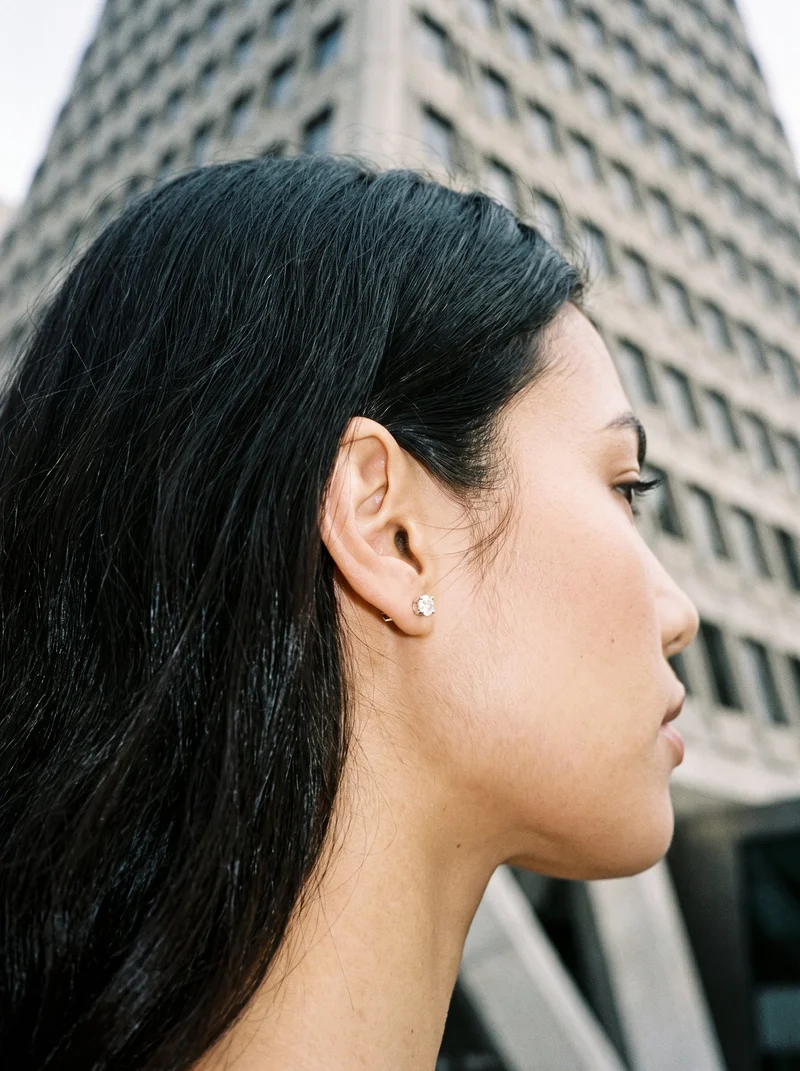 A 19-year-old Arab woman is shown in a head crop from an angled rear view with her head level, highlighting a women's diamond stud earring. A pyramid building low-angle backdrop is visible.