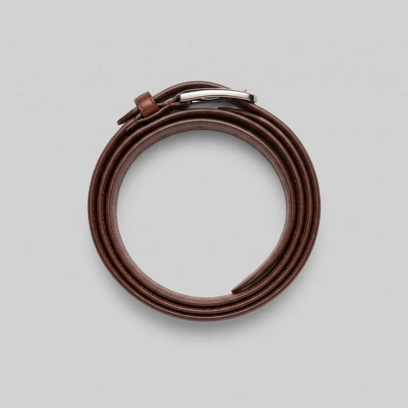 A brown dress belt is shown coiled flat into a circular shape. Its smooth grained strap has rounded finished edges, while the polished metal buckle, curved rectangular frame, visible prong, and fixed keeper loop appear near the top. The tapered strap tip is visible inside the coil.