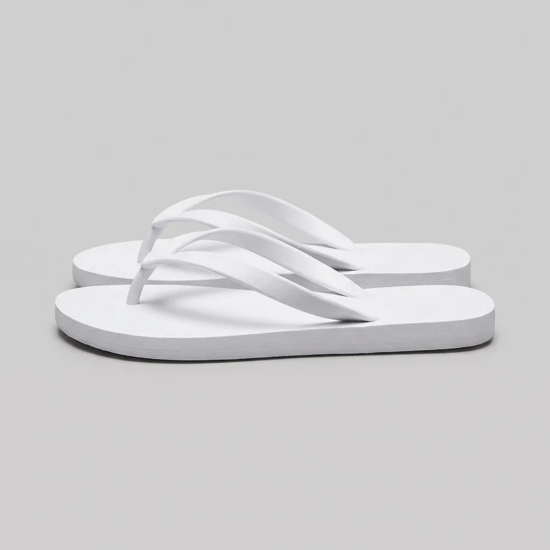 A pair of white thong flip-flop sandals is shown as a standalone product from a low side three-quarter angle. The sandals have flat, low-profile slab-style soles, rounded open toes, open backs, and broad smooth Y-shaped straps with toe posts. The flat footbeds and slightly textured sole edges are mostly visible.