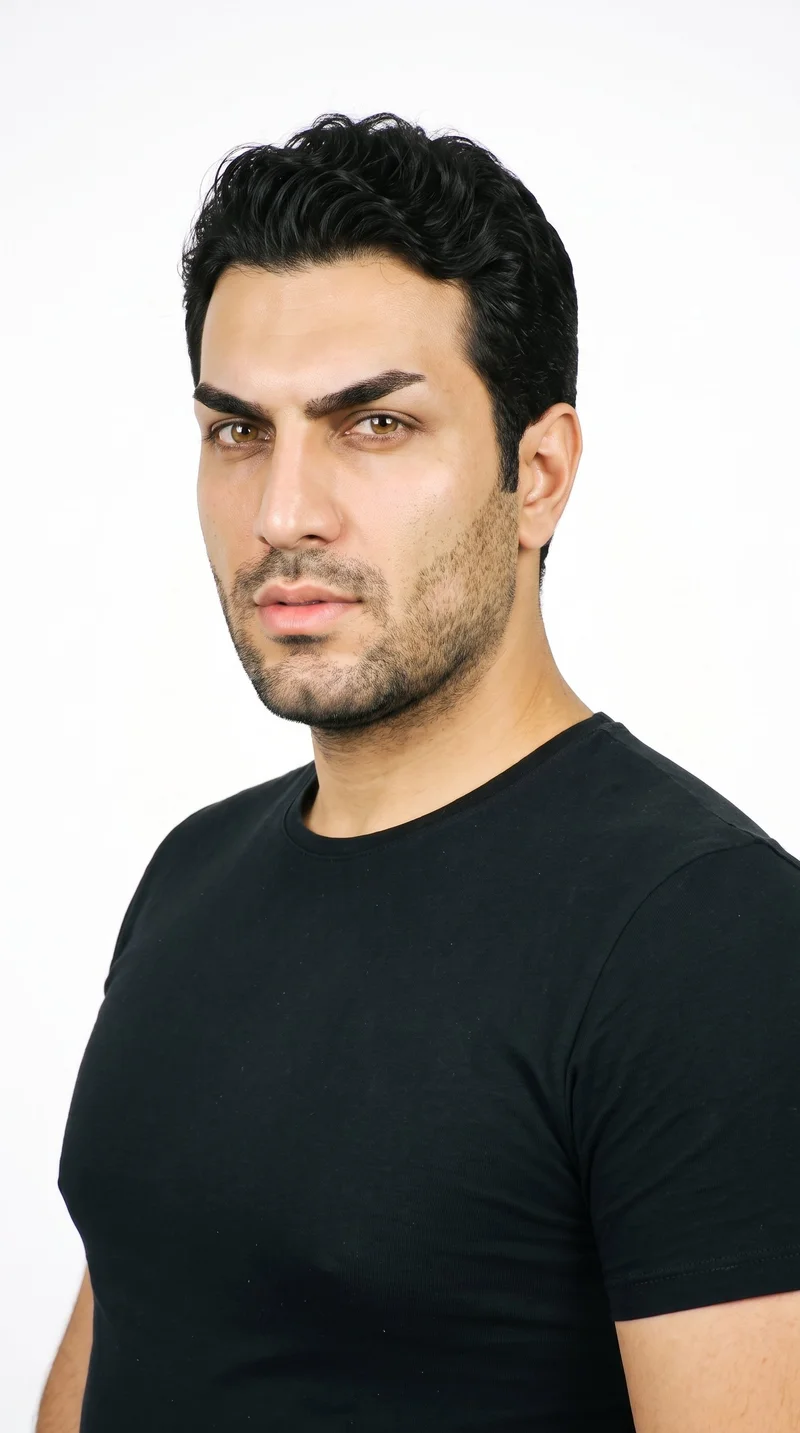 A 35-year-old Turkish man with medium olive skin and a neutral, greenish-golden undertone. His face is sharp and angular, with a defined jaw and pronounced cheekbones. He has medium-thickness eyebrows, amber eyes with a golden tone, and full lips. His deep black hair falls in soft waves, and he has short, even three-day beard growth with a closely groomed texture.