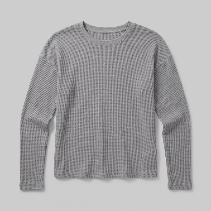 A mostly complete front view of a grey waffle-knit long-sleeve crewneck shirt shown as a standalone product. It has a straight silhouette, dropped shoulder seams, full-length sleeves with stitched cuffs, a straight stitched hem, and a raised ribbed neckband.