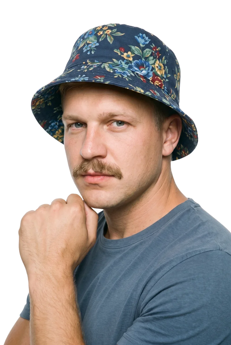 A 41-year-old Slavic man is shown from the bust up at a front three-quarter angle, wearing a men's floral print bucket hat. His wrist is held at his jaw, and he has a neutral facial expression. The subject is set against a pure white backdrop.