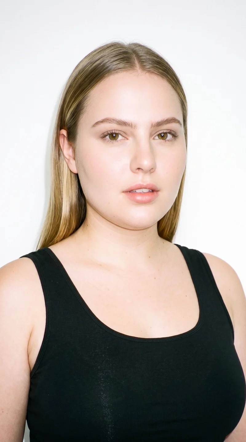 A 22-year-old Caucasian woman with fair skin and a neutral undertone has an inverted-triangle face, with a wider forehead narrowing toward the chin. She has thick eyebrows, hazel eyes with green-gold flecks, and thin lips. Her dark-blonde hair is straight, smooth, and divided evenly at the centre.