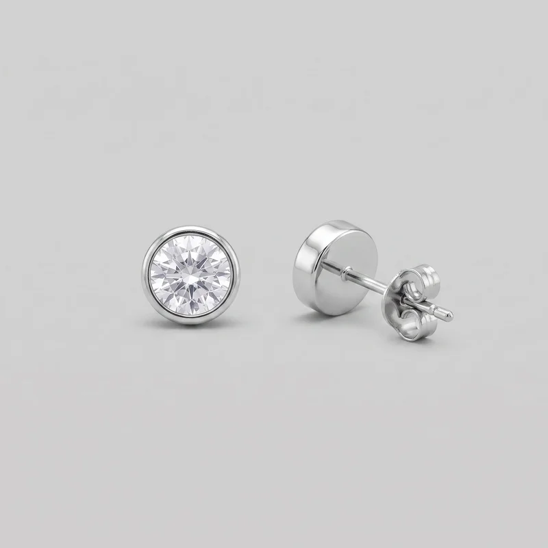A pair of round stud earrings is shown as a standalone product, with one earring facing forward and the other angled to reveal its side, straight post, and butterfly clutch backing. Each earring has a circular faceted center set inside a raised smooth bezel rim, with no visible logos, text, or additional embellishments.