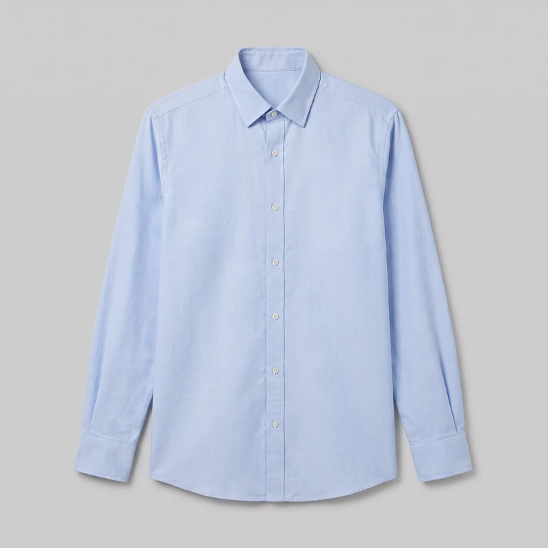 A light blue Oxford shirt is shown laid flat in a complete front view. It has a pointed spread collar, long sleeves with barrel cuffs, a full button placket, shoulder yoke seams, topstitched collar and placket edges, evenly spaced front buttons, and a slightly curved shirt-tail hem. No chest pockets or visible logos, prints, patches, embroidery, or embellishments are present.