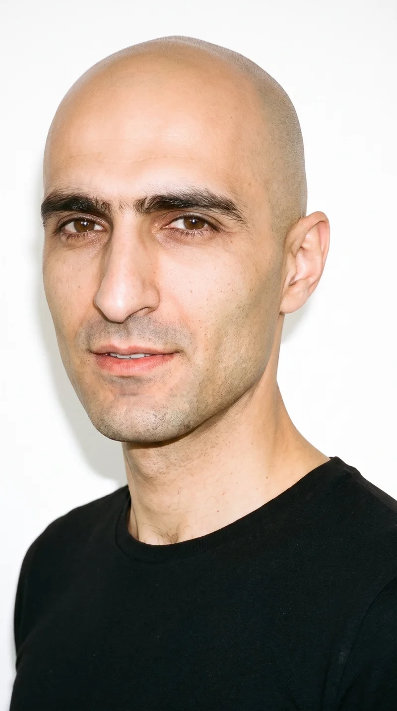 A 37-year-old Slavic man with a light porcelain skin tone and cool undertone. His weathered face has characterful, lived-in features with strong definition, thick eyebrows, brown eyes, and full lips. He has a bald scalp with no hair, and his face is clean-shaven with no facial hair.