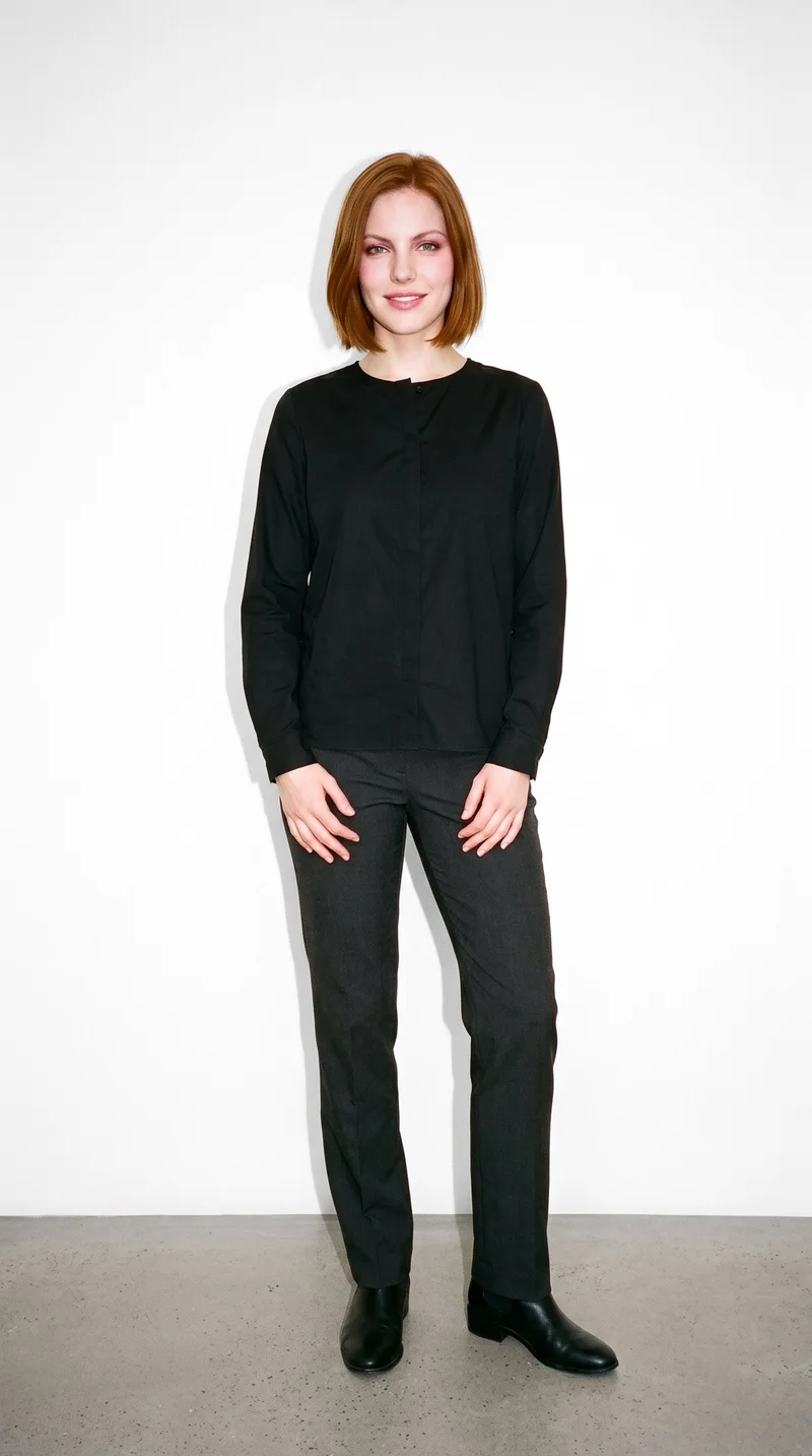 A 26-year-old Caucasian woman wears a black classic blouse in a full-body front view. She is smiling with her hands held in front of her against a pure white studio backdrop.