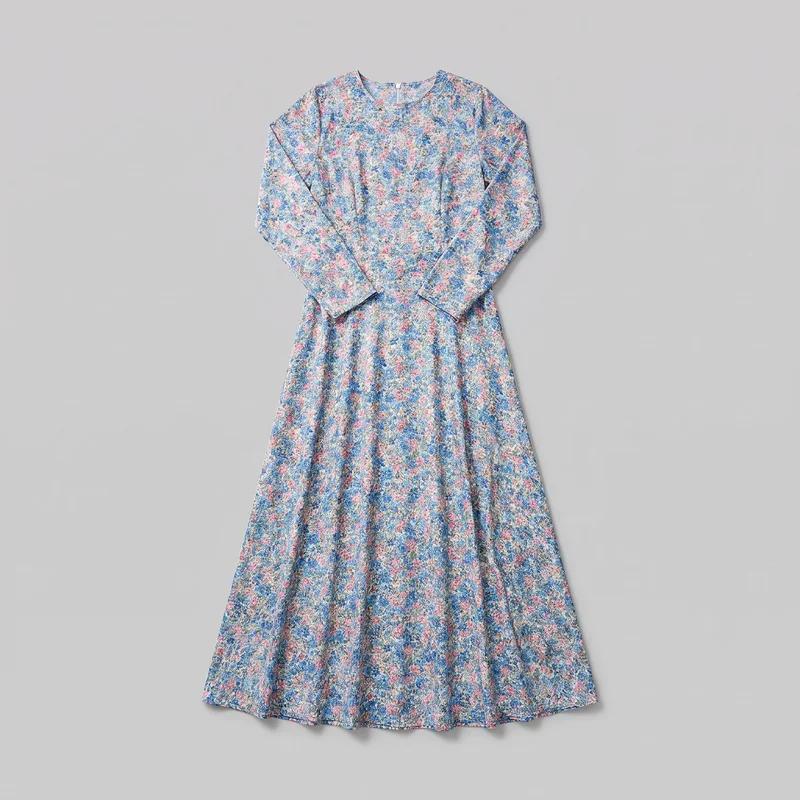 A complete women's floral print modest maxi dress is laid flat, showing its round neckline, long sleeves with straight cuffs, fitted bodice, defined waist seam, vertical bodice shaping, and flared A-line skirt extending to a softly wavy hem. The dense all-over small floral print covers the exterior, and a short center-back zipper is visible at the neckline.