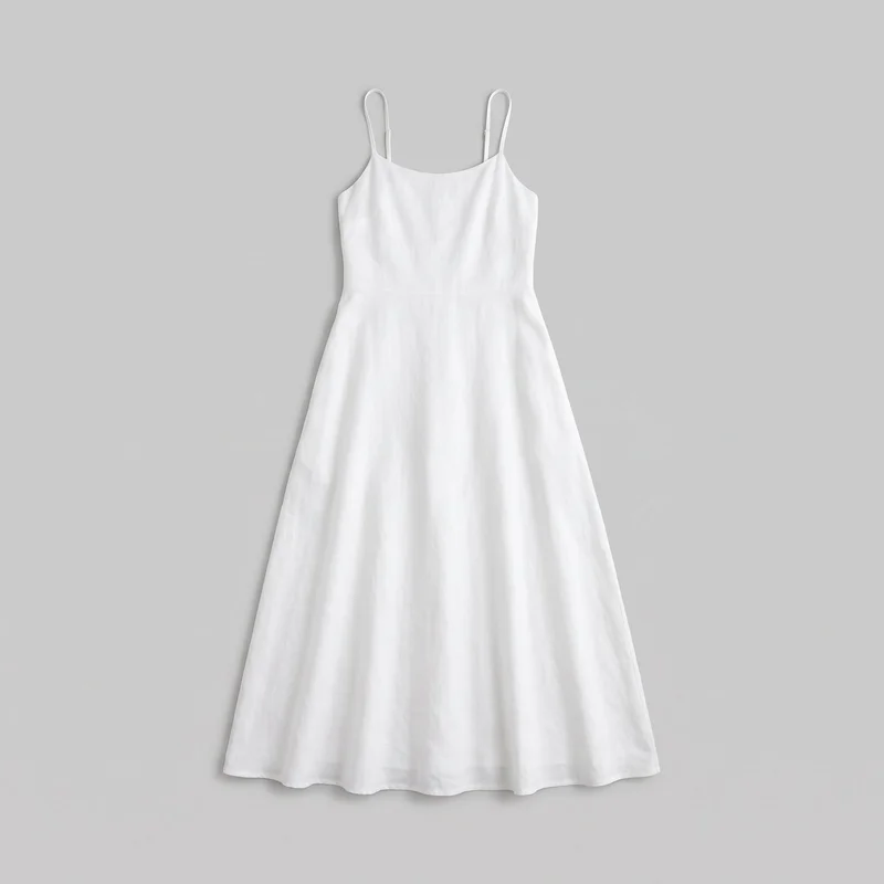 White linen women's maxi dress shown laid flat in a complete front-facing view. The sleeveless dress has slim spaghetti straps with visible adjusters, a shallow scoop neckline, a tailored bodice that narrows at the waist, a defined horizontal waist seam, softly shaped side seams, and a flared A-line skirt extending to a full-length straight hem with slight natural waviness. No logos, prints, patches, embroidery, or embellishments are visible.