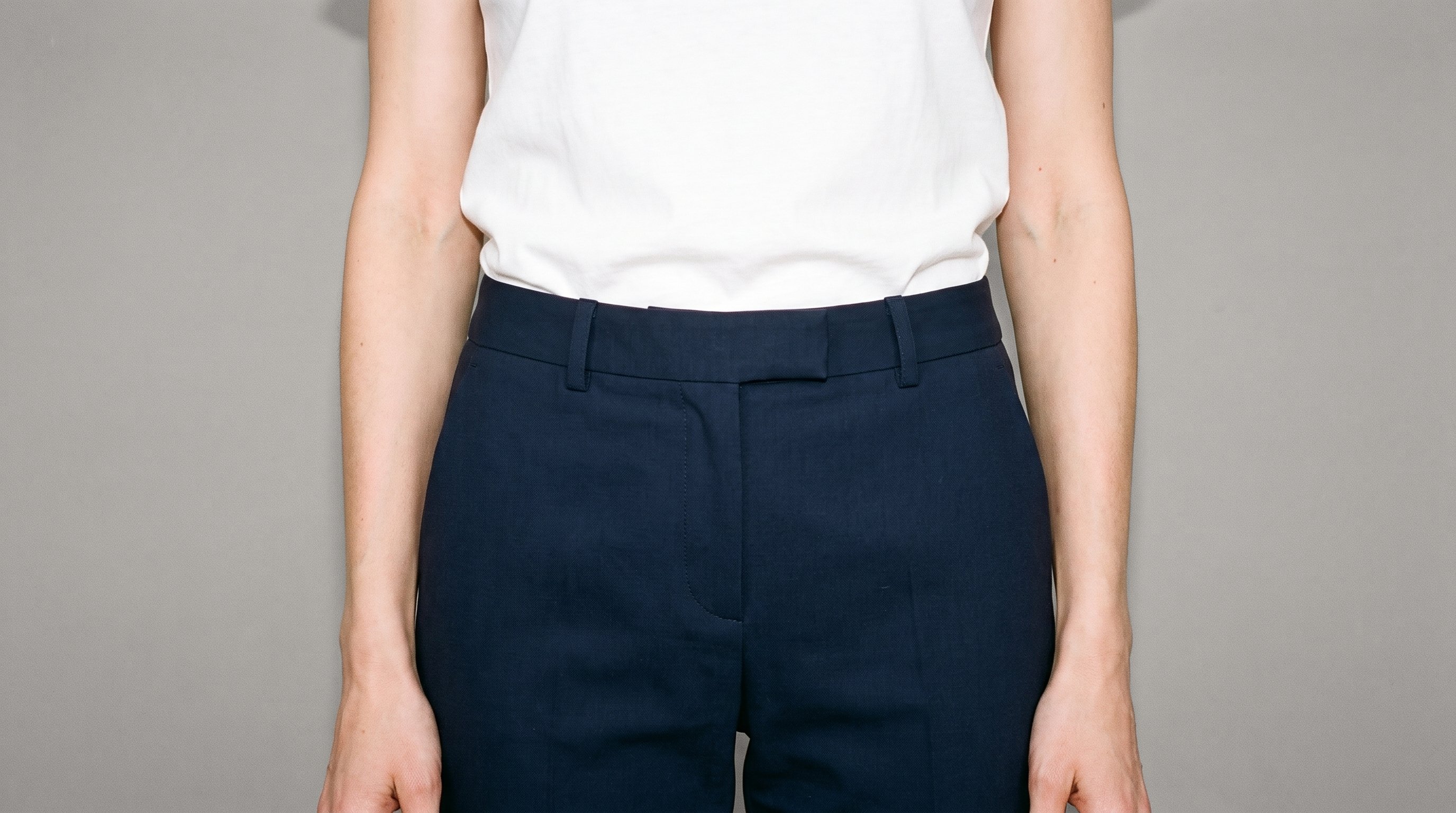 Women's navy wool suit trousers shown from the front in a hips-level crop, with the hips level and the garment set against a Couture Grey studio-wall backdrop.