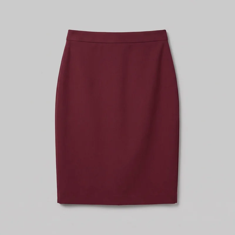 A burgundy women's tailored pencil skirt is shown alone in a complete front view. It has a slim, straight silhouette that tapers subtly toward a straight knee-to-midi hem, with a wide smooth waistband, a horizontal seam below the waistband, plain front paneling, and lightly shaped side edges. No pockets, closures, vents, pleats, gathers, logos, prints, patches, embroidery, or embellishments are visible.