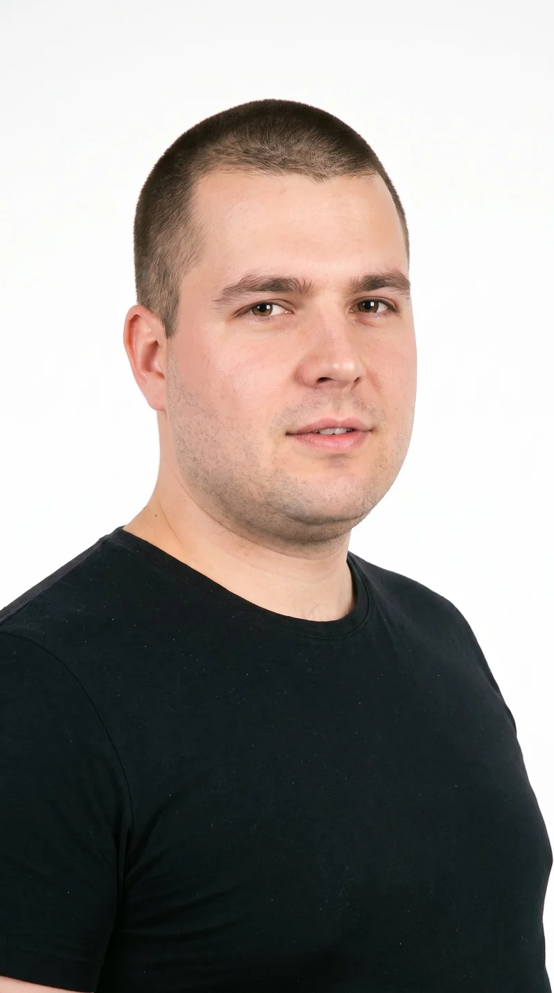 A 34-year-old Caucasian man with fair skin and a peach undertone has a triangular face with a wide jaw narrowing toward the forehead. His medium-thickness eyebrows frame brown eyes, and he has full lips. His dark-brown hair is clipped very short and evenly in a buzz cut, and his face is clean-shaven with smooth skin across the whole face.