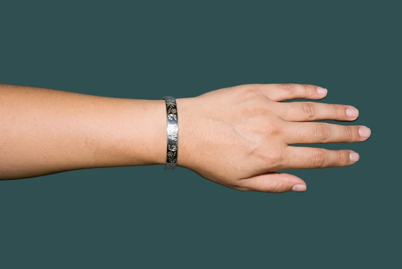 A woman's hand and wrist are shown from above with the hand held flat, wearing an engraved cuff. The image is framed tightly around the hand and wrist against a dark slate backdrop.