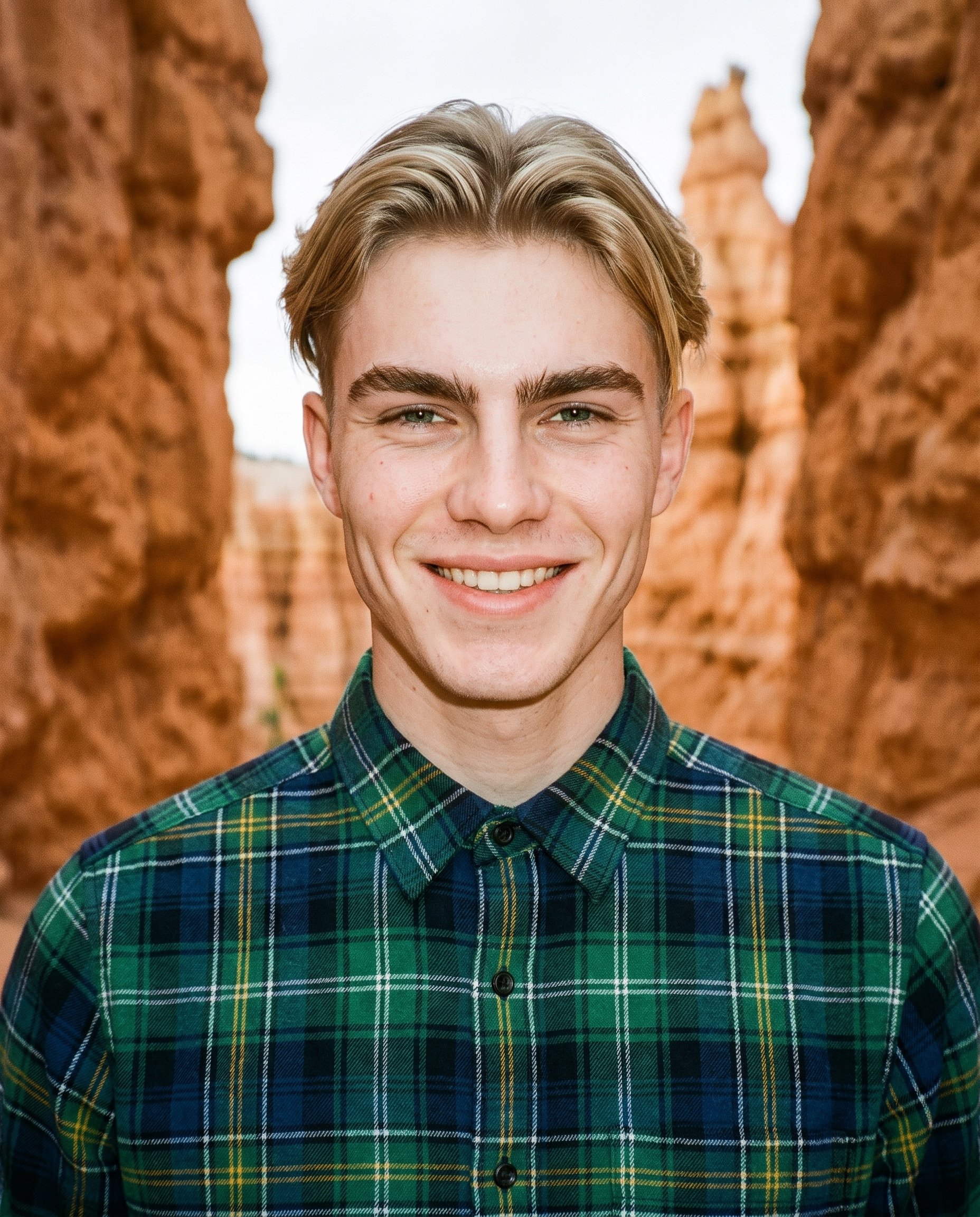 A 19-year-old Caucasian man wears a green plaid flannel shirt in a front-facing bust view. His head is level with a natural expression, and Bryce Canyon hoodoos form the backdrop.