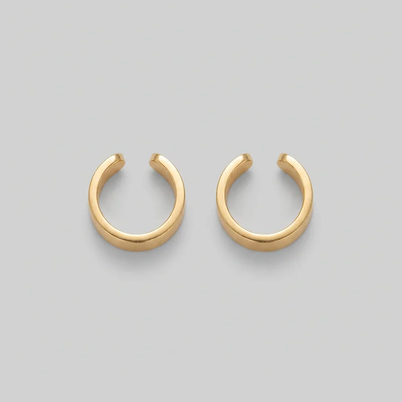 A matching pair of gold open C-shaped hoop earrings is shown as standalone product objects from above at a slight angle. Their full silhouettes reveal smooth rounded tubular profiles, slightly thicker lower curves, tapering blunt open ends, and subtle beveled edges along the inner sides. No posts, clasps, logos, prints, or embellishments are visible.