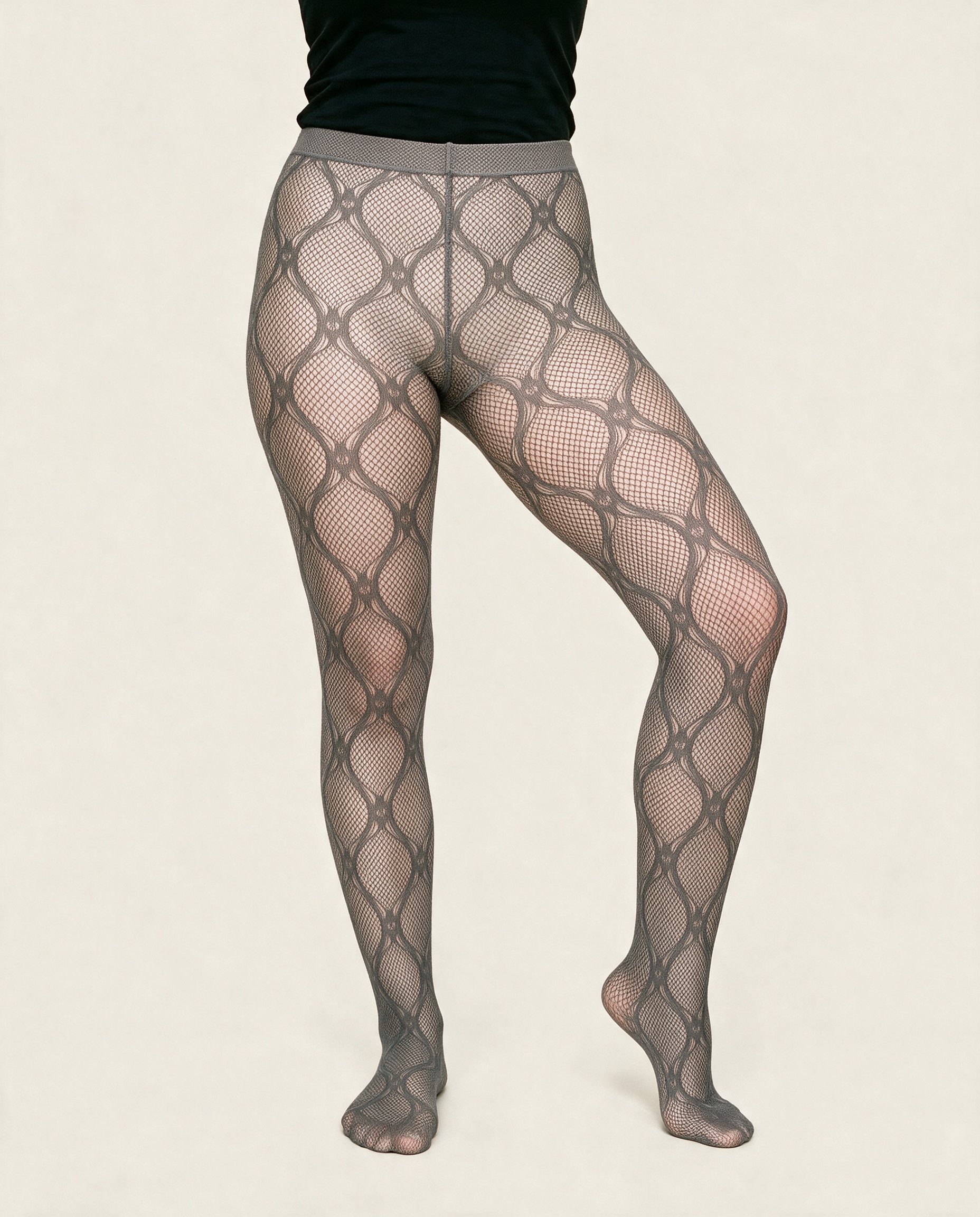 Patterned fishnet tights worn on a female model’s lower body, shown from the front with one heel lifted. The alabaster flat-color backdrop keeps the focus on the tights.