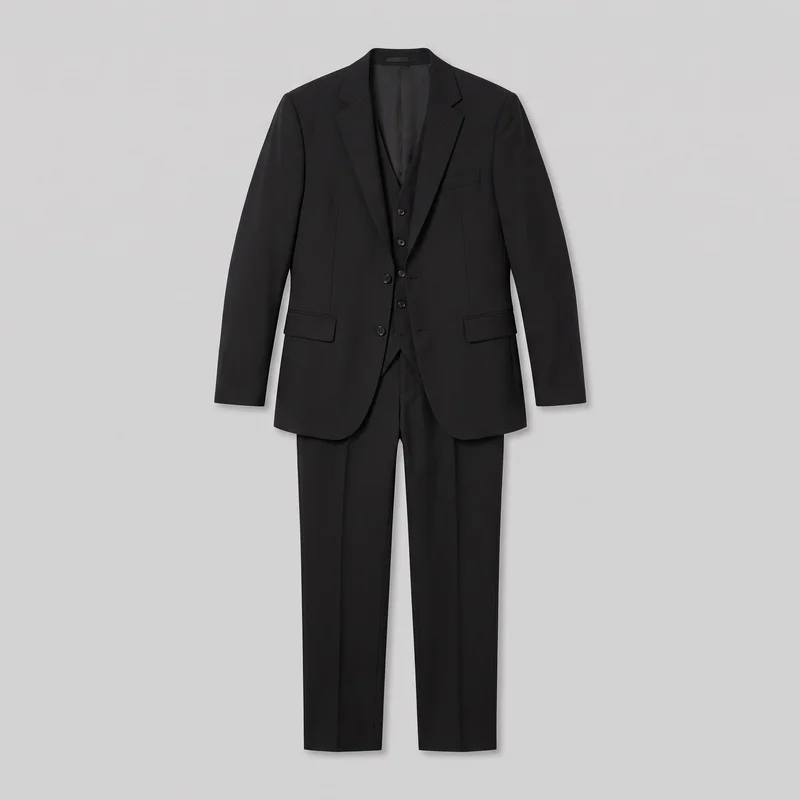 A black men’s three-piece suit is shown front-facing as a standalone product, with the jacket arranged over a buttoned waistcoat and matching full-length trousers. The jacket has notch lapels, a visible button and buttonhole, a welt breast pocket, flap waist pockets, and structured shoulders. The trousers have a flat front, pressed center creases, and straight hems, with the full legs visible.