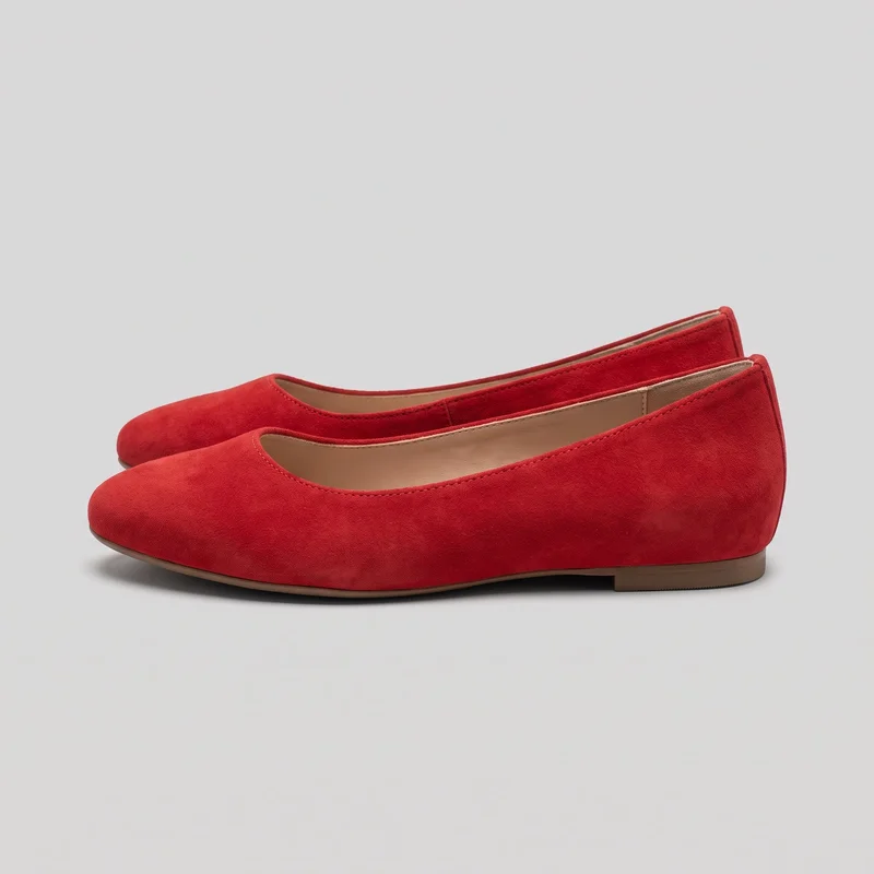 A pair of red ballet flats is shown in a side-angled standalone view, with one shoe positioned in front of the matching shoe. The shoes have slip-on, closed-toe designs with rounded toes, shallow vamp openings, low-cut sides, stitched binding along the toplines, thin visible sole edges, and low rectangular heels.