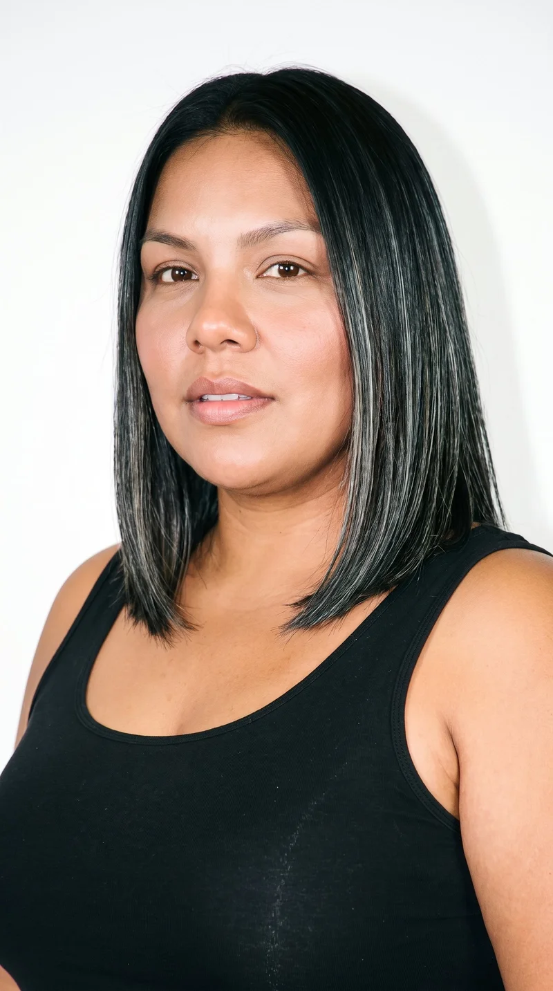 A 36-year-old Hispanic woman with medium-brown skin and a neutral undertone. Her angular face has sharp, defined cheekbones and jawline, framed by thick eyebrows and green eyes. She has full lips and deep black hair styled in a long bob that falls between the chin and shoulders.