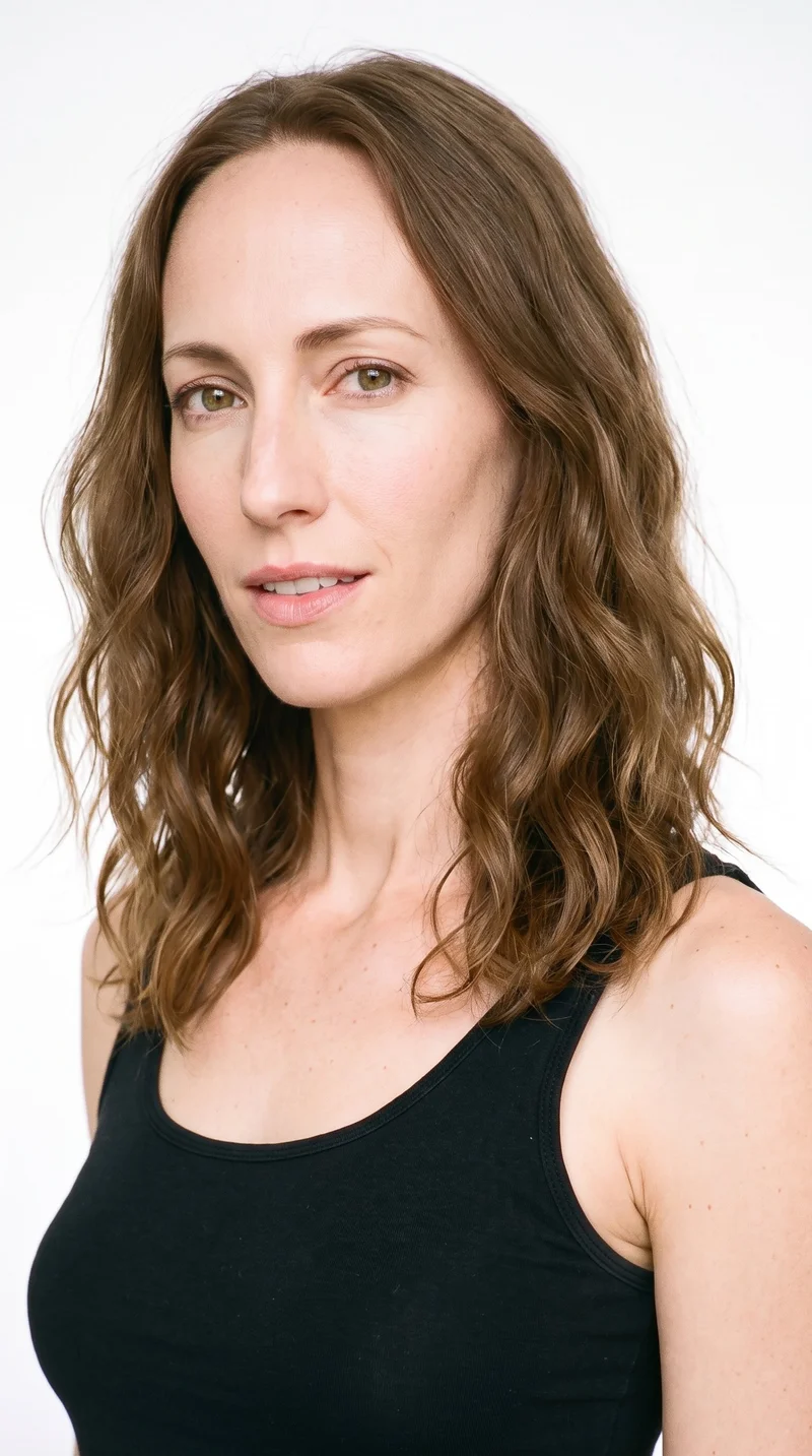 A 35-year-old Caucasian woman with fair skin and a peach undertone. Her face is long, with more length than width, a tall forehead, and elongated cheeks. She has thick eyebrows, hazel eyes with green-gold flecks, and medium lips. Her medium-brown hair falls in loose, slightly tousled waves with natural volume.