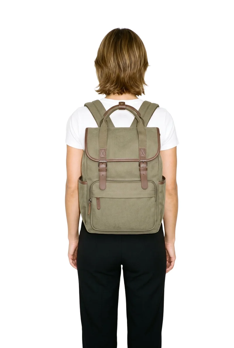A 31-year-old Caucasian woman is shown from the rear in a three-quarter-length view, carrying a women's olive utility backpack on her back. The backpack is the main focus against a pure white backdrop.