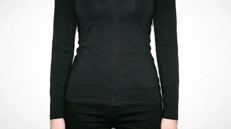 A woman wearing a black compression base layer is shown from the hips up in a front view with her hips level. The garment is presented against a pure white studio backdrop.