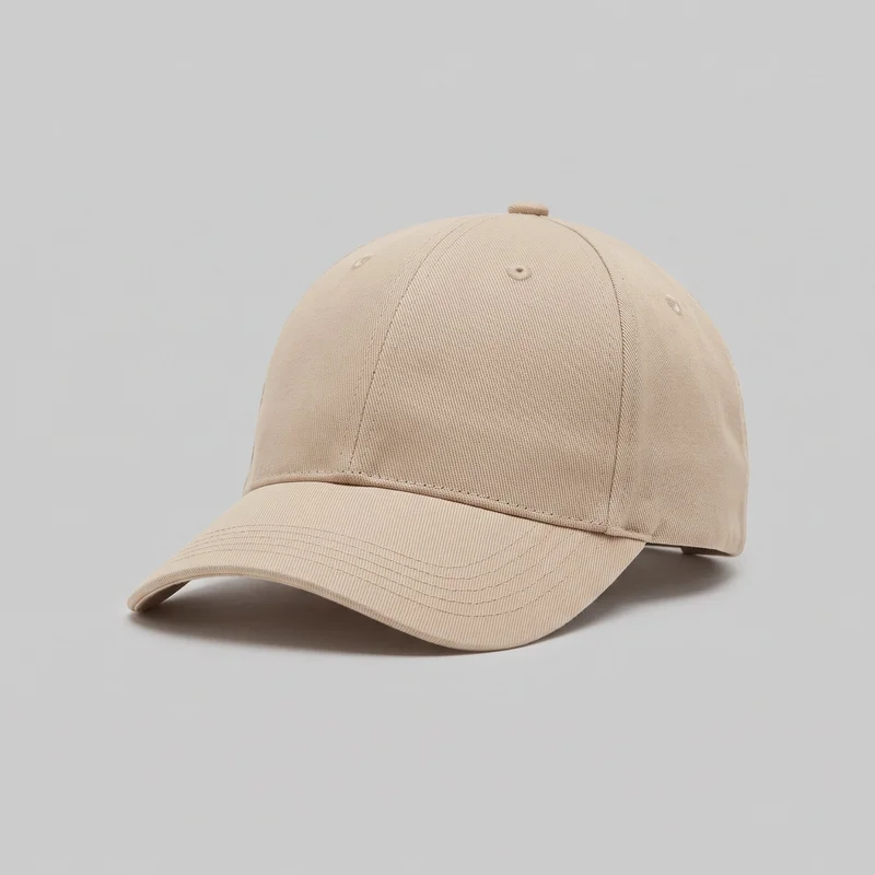 A standalone beige baseball cap is shown from a front three-quarter angle. It has a structured rounded crown divided into vertical panels with visible seam stitching, a covered top button, embroidered ventilation eyelets, and a curved brim with parallel rows of topstitching. No logos, prints, patches, or decorative embellishments are visible.
