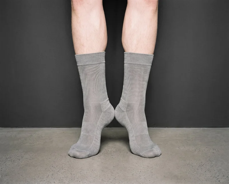 Both feet wear men's grey performance socks in a front view, with both heels lifted. A charcoal slate backdrop fills the studio setting.