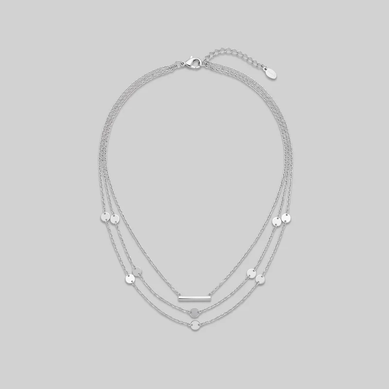 A silver multi-strand necklace is laid in an oval shape. Fine link chains form layered, graduated drapes with repeated flat round disc stations, a narrow horizontal bar pendant, and two lower circular disc drops; the clasp and extension chain are positioned at the top.
