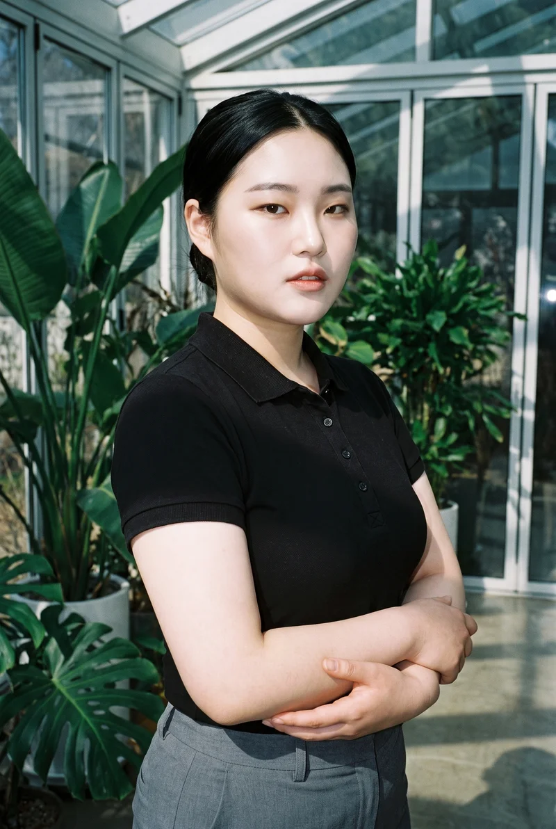 An 18-year-old Korean woman is shown from the upper body wearing a black polo shirt. She faces the camera at a front three-quarter angle with her forearms folded and a serious expression. A sunroom serves as the backdrop.